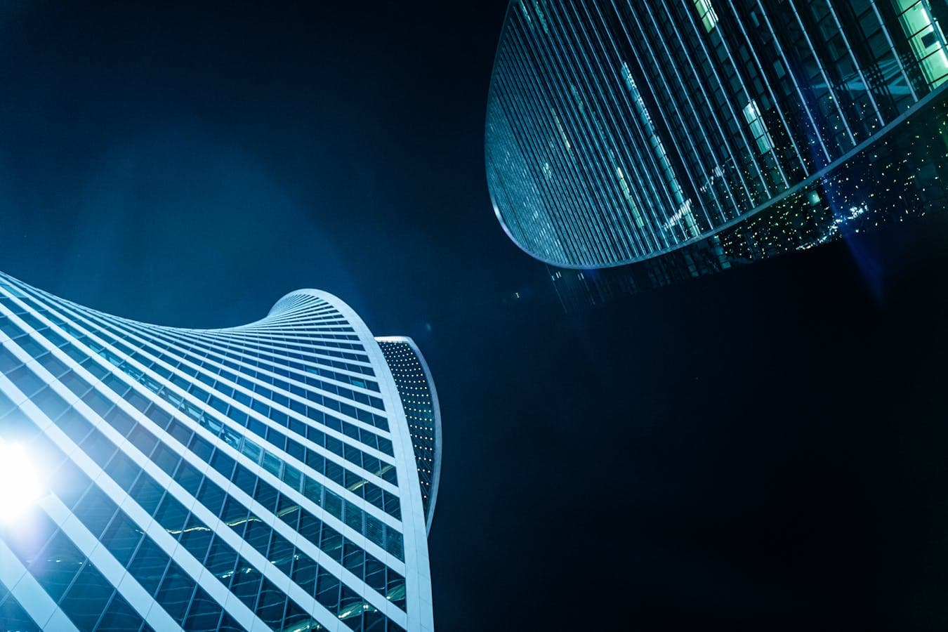 Nighttime skyscrapers with sleek architecture and illuminated glass facades, suitable for a premium futuristic brand backdrop.